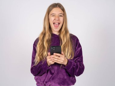 Heyecanlı, mor süveter giyen, göz kırpan, akıllı telefon kullanan sosyal ağ haberlerini okuyan güzel bir kız. 