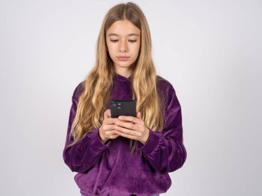 Mor kazak giyen güzel bir kız sosyal medya haberleri ya da önemli e-postalar okuyan akıllı telefon kullanıyor. 