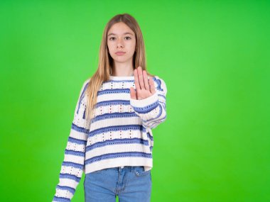 Yeşil stüdyo arka planında çizgili süveter giyen güzel bir genç kız dur işaretini gösteriyor.