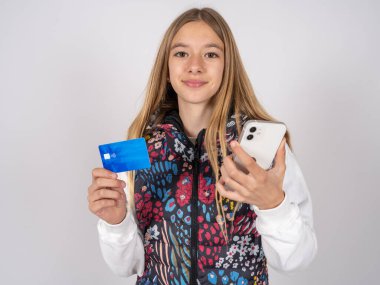 Renkli yelek giyen güzel bir kız kulaklarına stereo kulaklık takıyor modern cep telefonu ve kredi kartı takıyor.