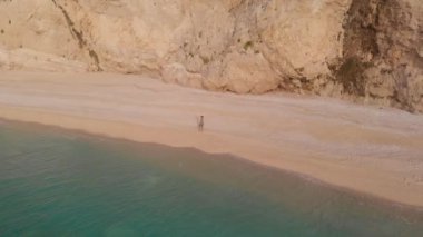 Yavaş çekim: Yunanistan 'da güzel boş bir plajda yürüyen ve dinlenen kadın görüntüsü. İyon adası Port Katsiki, Lefkada 'daki dramatik sahil manzaralı kayalık uçurumlar.