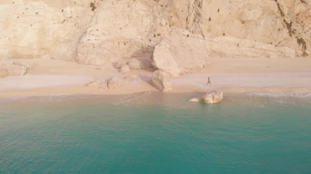 ゆっくりとした動き ギリシャの美しい空のビーチで歩いてリラックスする女性の空中ビュー イオニア島の劇的な海岸線の風光明媚な湾岩の崖 ポートカチキ レフナ ストック映像