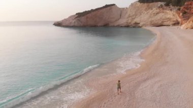Yavaş çekim: Yunanistan 'da güzel boş bir plajda yürüyen ve dinlenen kadın görüntüsü. İyon adası Port Katsiki, Lefkada 'daki dramatik sahil manzaralı kayalık uçurumlar.