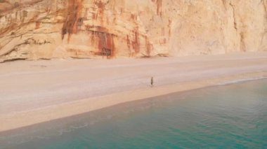 Yavaş çekim: Yunanistan 'da güzel boş bir plajda yürüyen ve dinlenen kadın görüntüsü. İyon adası Port Katsiki, Lefkada 'daki dramatik sahil manzaralı kayalık uçurumlar.
