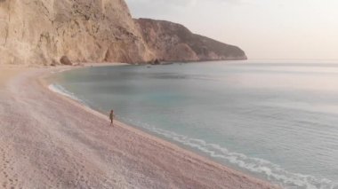 Yavaş çekim: Yunanistan 'da güzel boş bir plajda yürüyen ve dinlenen kadın görüntüsü. İyon adası Port Katsiki, Lefkada 'daki dramatik sahil manzaralı kayalık uçurumlar.