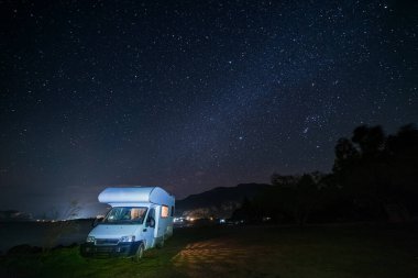 Yıldızlarla dolu bir gökyüzü altında huzurlu bir gece karavanı üzerinde sakin bir göl kenarında, mükemmel bir karavanı gözler önüne seriyor.