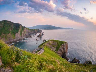 Gaztelugatxe 'nin arkasında gün batımı Bask Ülkesi İspanya dolambaçlı taş köprüsü inzivaya çekilen kayalık adaya doğru tırmanıyor sakin deniz parlayan gökyüzü antik yol mistisizm inanç sonsuz yalnızlık yolculuğu