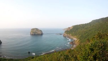 Gaztelugatxe 'nin arkasında gün batımı Bask Ülkesi İspanya dolambaçlı taş köprüsü inzivaya çekilen kayalık adaya doğru tırmanıyor sakin deniz parlayan gökyüzü antik yol mistisizm inanç sonsuz yalnızlık yolculuğu