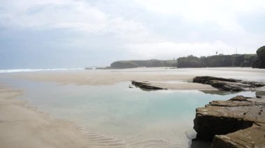 Katedrais sahili Galiçya 'da sular çekildiğinde İspanya kumtaşı gelgit havuzlarını gökyüzü kayalıklarını yansıtan geniş kayalıklar parlak ışık altında barışçıl doğal merak altında uzanır.