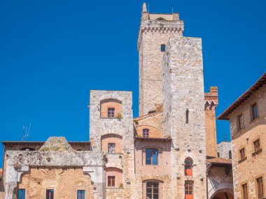 San Gimignano İtalya 'nın ortaçağ kuleleri mavi gökyüzüne karşı tarihi mimari terasotta çatılarının üzerinde yükselen canlı sokak manzaraları dikey kültür dikey gücünü yakalıyor.