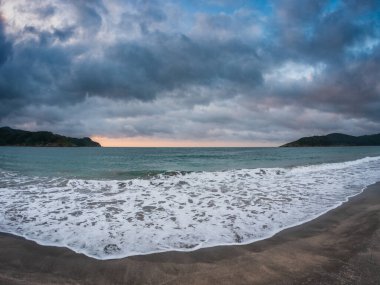 İspanya 'nın Galiçya kentindeki Atlantik kıyısını aydınlatan dramatik alacakaranlık, sakin dalgaların üzerinde süzülen kara bulutlar ıssız bir kumsalda ıssızlığı ve içselliği simgeliyor.