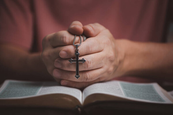 Open holy bible book with people hands folding and holding cross necklace in the middle book pray to God