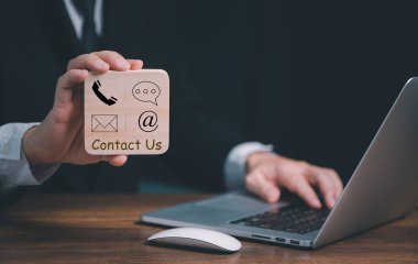 CONTACT ABD, İşadamı Eli posta, telefon, e-posta, sohbet simgeleri ile ahşap blok tutuyor. Ticari müşteri desteği ve hizmet kavramı, kopyalama alanı.