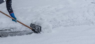 Genç adam kışın yürüyüş yolundan kar kürüyor.