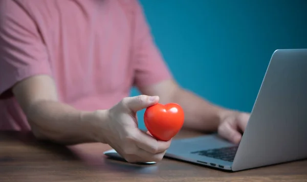 Red Heart 'ı tutan ve dizüstü bilgisayar kullanan adam bağış, sigorta, aşk sohbeti online randevu kavramı.