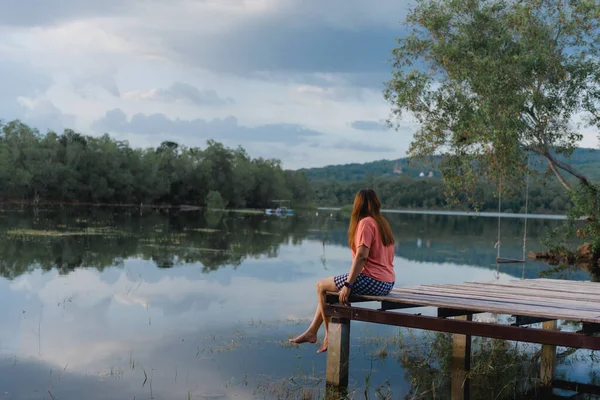 午前中に湖の桟橋に座っている旅行者の女性は リラックスして美しい山の景色を楽しんで — ストック写真