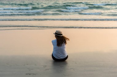 Şapka takan, kumsalda oturan güzel Asyalı kadın yaz tatilinde mutlu tatil konsepti..