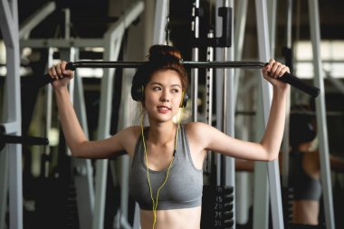 Genç Asyalı sağlıklı ve gülümseyen kadın portresi spor salonunda ağırlık kaldırma ekipmanıyla çalışıyor..