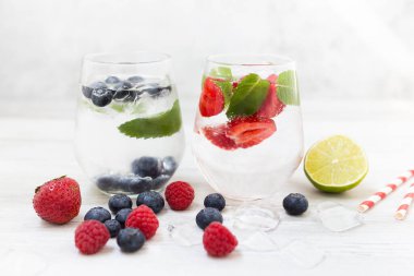 Beyaz arka planda çilek ve yaban mersinli bir bardakta maden suyu ve kopyalama alanı. Yazın ferahlatıcı bir içecek.. 