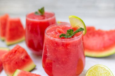 Dilimlenmiş meyve, nane ve limon yapraklı karpuz içecekleri beyaz ahşap arka planda. Yazın ferahlatıcı bir içecek.. 