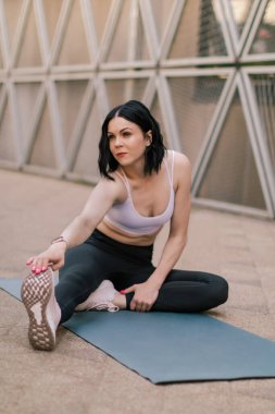Sporcu kadın dışarıda esneme ve yoga egzersizleri yapıyor. Şehir merkezindeki açık hava koşusundan sonra esneme hareketleri yapan bir kadın. Sağlıklı spor yaşam tarzı.
