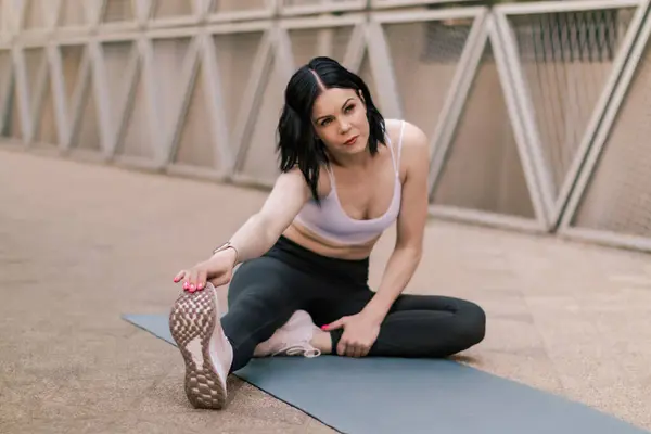 Sporcu kadın dışarıda esneme ve yoga egzersizleri yapıyor. Şehir merkezindeki açık hava koşusundan sonra esneme hareketleri yapan bir kadın. Sağlıklı spor yaşam tarzı.
