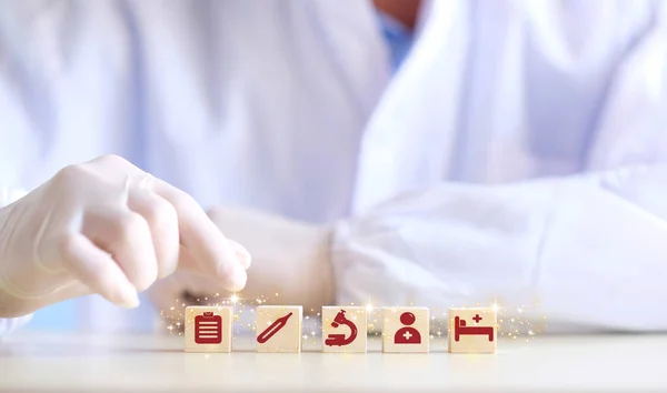 Doctor arranging and stacking wooden block cubes with printed screen health care and medical icons for the concept of health and wellness. Hand-arranging a wood block with a medical icons.