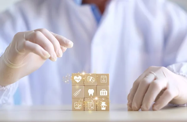 Doctor arranging and stacking wooden block cubes with printed screen health care and medical icons for the concept of health and wellness. Hand-arranging a wood block with a medical icons.