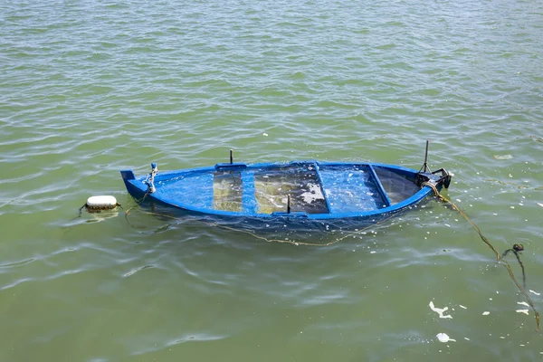 A small blue boat sinking into the sea