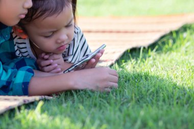 Çimenlerde uzanmış telefonlarına bakan iki genç kız, yaz, altın saat, gün batımı. SSTKHome
