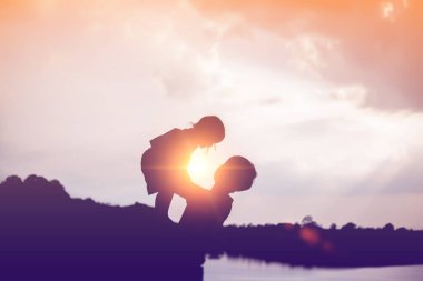 Açık havada mutlu, genç ve uyumlu bir ailenin silueti. Yazın gün batımında gülüp oynuyorlar.