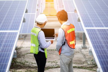 Erkek mühendisler çatıdaki elektrik santralinin fotovoltaik panellerini kontrol ediyorlar.