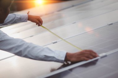 Fotovoltaik güneş panellerini mezurayla ölçen insan ellerine yaklaş. Erkek işçi, fotovoltaik etki yoluyla elektrik üretmek için güneş modülleri kurmadan önce ölçümler alıyor.