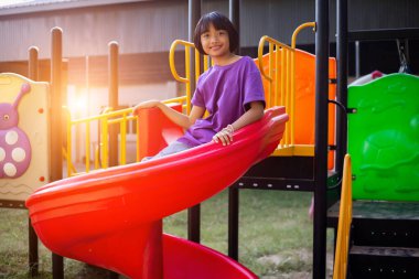 Neşeli çocuklar güneşli bir öğleden sonra oyun parkında kayıyor.