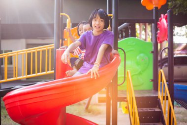 Neşeli çocuklar güneşli bir öğleden sonra oyun parkında kayıyor.