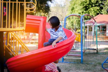 Neşeli çocuklar güneşli bir öğleden sonra oyun parkında kayıyor.
