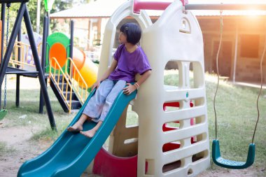 Neşeli çocuklar güneşli bir öğleden sonra oyun parkında kayıyor.