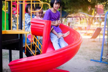 Neşeli çocuklar güneşli bir öğleden sonra oyun parkında kayıyor.