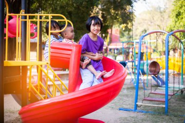 Neşeli çocuklar güneşli bir öğleden sonra oyun parkında kayıyor.