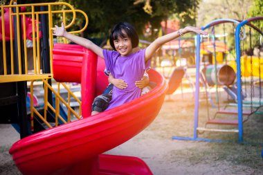 Neşeli çocuklar güneşli bir öğleden sonra oyun parkında kayıyor.