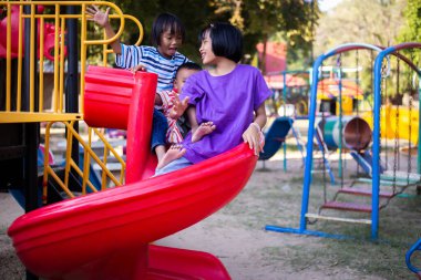Neşeli çocuklar güneşli bir öğleden sonra oyun parkında kayıyor.