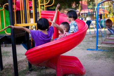 Neşeli çocuklar güneşli bir öğleden sonra oyun parkında kayıyor.