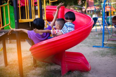 Neşeli çocuklar güneşli bir öğleden sonra oyun parkında kayıyor.