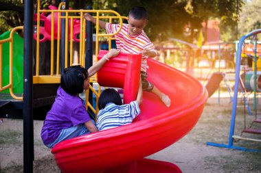 Neşeli çocuklar güneşli bir öğleden sonra oyun parkında kayıyor.
