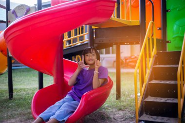 Neşeli çocuklar güneşli bir öğleden sonra oyun parkında kayıyor.