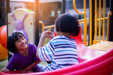 Neşeli çocuklar güneşli bir öğleden sonra oyun parkında kayıyor.
