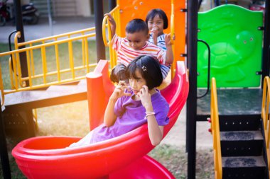 Neşeli çocuklar güneşli bir öğleden sonra oyun parkında kayıyor.