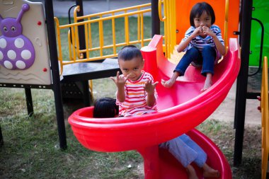 Neşeli çocuklar güneşli bir öğleden sonra oyun parkında kayıyor.