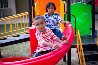 Neşeli çocuklar güneşli bir öğleden sonra oyun parkında kayıyor.