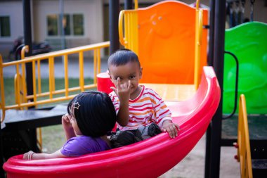 Neşeli çocuklar güneşli bir öğleden sonra oyun parkında kayıyor.
